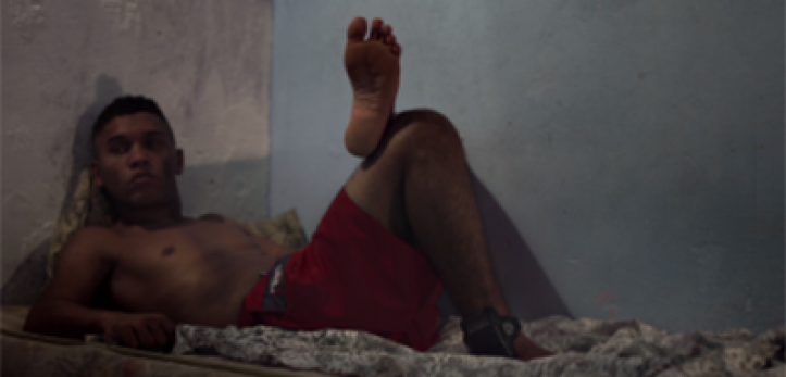 Cena do filme, Ivan está deitado em um colchão com a tornozeleira de monitoração eletrônica