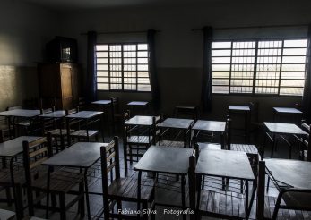 Na foto há uma sala de aula iluminada apenas pela luz das janelas e carteiras vazias. Foto: Fabiano Silva Fotografia
