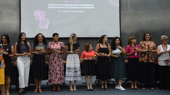 As vencedoras do Prêmio do Selo de Direitos Humanos e Diversidade na categoria "Mulheres" estão de pé no palco, segurando os troféus e sorrindo.